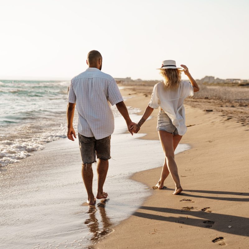 Young beautiful couple walking on beach near sea at sunset